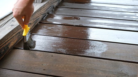 Close-up of a brush painting wood floor in brown color. Wood plank impregnation. Finish oil coating of board. Second layer of oiling. Manual construction work in a gazebo. Naturalの写真素材