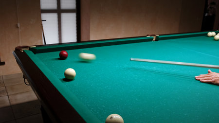 Russian billiards on a green table. American billiard. A player hits the white ball with a cue rolling a red ball into the pocket. Successful shot. Pastime at home playing sportの写真素材