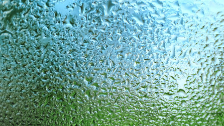 Water Drops on a glass. Dripping rain drops textured background. Close up of misted window with droplets draining down. Increased air humidity. Rainy weather. Blue green colorsの写真素材