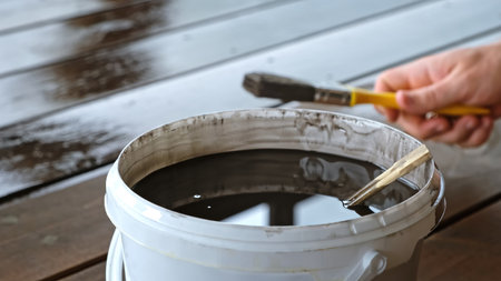 Close-up of bucket of brown paint. A person's hand oiling a wooden floor. Drying oil. Painting work. Impregnating boards. Varnish finish coating. Manual work. Side viewの写真素材