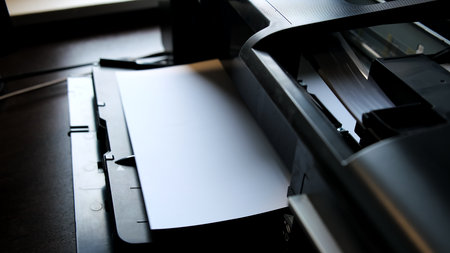 A printed paper sheet comes out of the color inkjet printer in close-up. Printing process. Printed a...