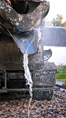 Water flows down the chute of a concrete mixer. Washes the concrete mixer after use. Washing away the remaining cement mixture. Cleaning of special vehicles. Dirty waterの写真素材