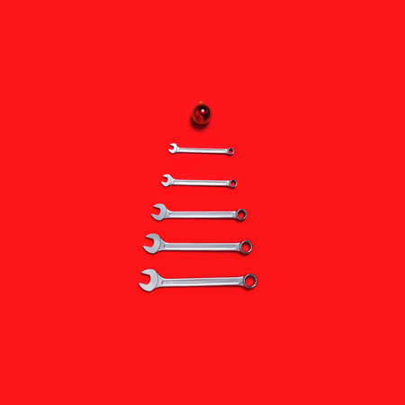 Christmas tree made of wrenches decorated with balls on a red background. New Year banner with tools. Postcard with place for greeting text for happy new year with industrialの写真素材