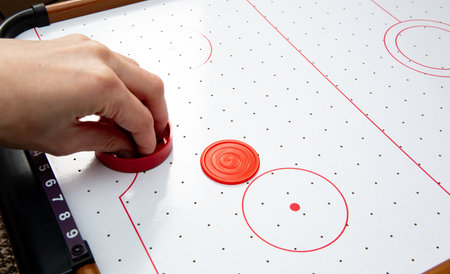 Hand ready to hit with paddle on puck. The portable table hockey includes plastic hockey paddles, a...