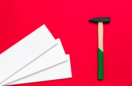 Hammer and white planks on a red background with place for text. Shop banner with construction tools, materials and instrument. New Year or Christmas holiday backdrop. Businessの写真素材