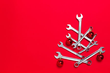 Creative christmas tree made of wrenches decorated with balls on red background. New Year banner with wrenches. Postcard with place for greeting text with industrial holidayの写真素材