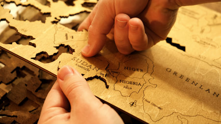 Male hands take out a laser-cut piece from a sheet of plywood to assemble a wooden decorative world map. The creative process of creating DIY crafts. Hobby concept. Carpentry. Highの写真素材
