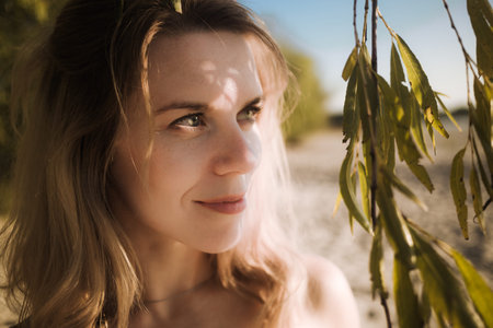 Close-up of blonde woman looking away near willow branches. Wild female nature. Sea vacation on...