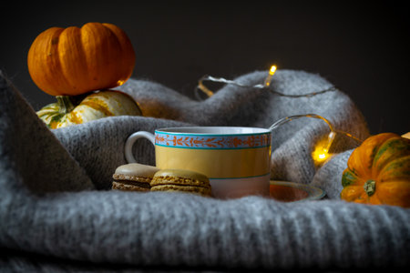 A cup of coffee and macaroons on the background of pumpkins and garland lights