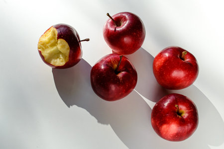 Five red ripe apples lying on a white table and their shadowsの写真素材