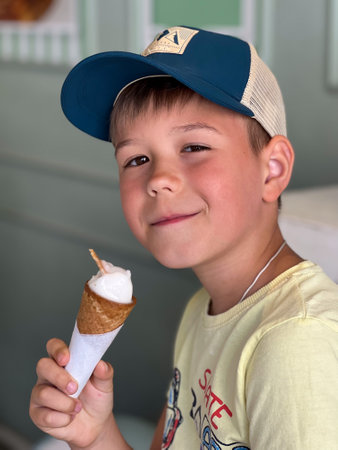 A boy in a yellow T-shirt and cap eats ice cream in a waffle coneの写真素材