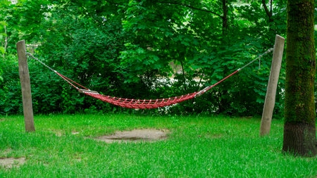 Large red hammock suspended on logs in a city park.の写真素材