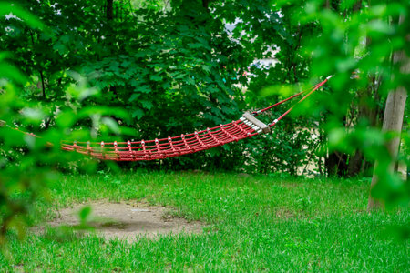 Large red hammock suspended on logs in a city park.の写真素材