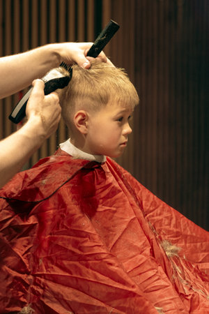 Little boy sitting at a haircut in a barbershop. Barber use scissor