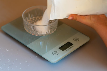 Weighing sugar from a pack on a kitchen scale.の写真素材