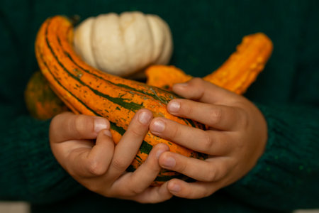 A child in a green sweater holds several colorful pumpkins in his hands.
