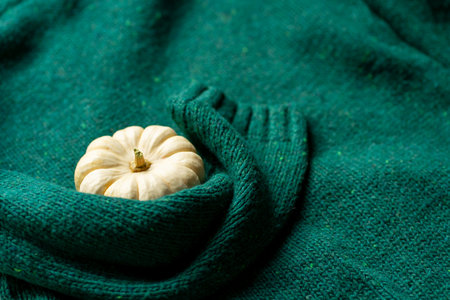 Orange pumpkin near a stack of knitted sweaters on a knitted blanket