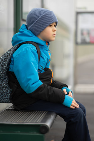 Boy with a backpack waits for a tram at a stop in the fog on the way to school.の写真素材