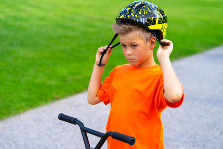 A young boy with blond hair and an orange T-shirt on a scooter.の写真素材