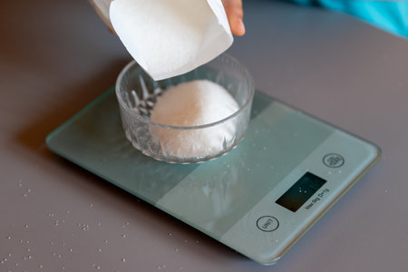 Weighing sugar from a pack on a kitchen scale.の写真素材
