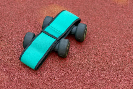Dumbbells and an elastic band for fitness lie on the sports ground.