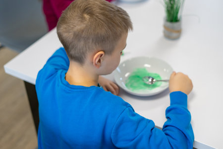 A boy in a blue jacket making green slime at a table in a white plateの写真素材