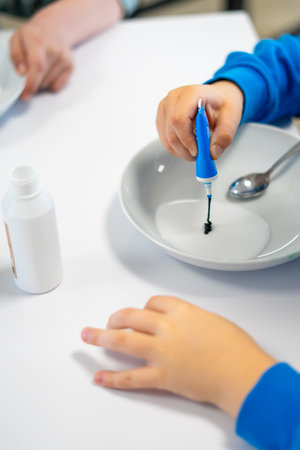 Children's hands squeeze blue dye into white glue to make slime.の写真素材