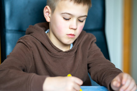 A boy in a brown jacket drawing with oil pencils while sitting at a table