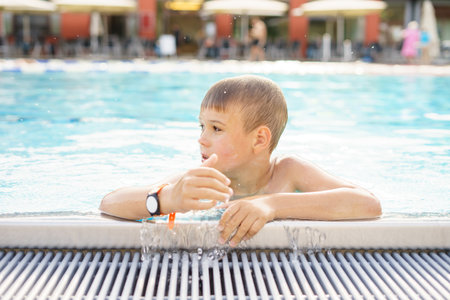Boy holding onto the side of a swimming pool, a boy swimming in an outdoor pool.