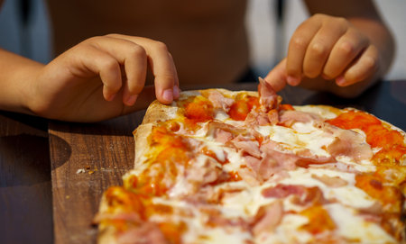 View of children's hands tearing a piece from a pinsa with cheese and ham.の写真素材