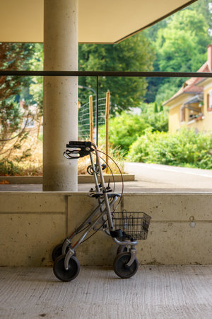Empty walker for the elderly with a basket parked against a concrete wall outdoors.の写真素材
