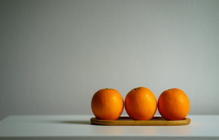 Three fresh ripe oranges on a small wooden tray on a white table. Still life of tropical fruitsの写真素材
