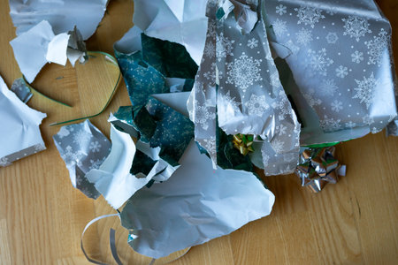 Torn green and silver paper taken from a Christmas present on the floor near the fir tree. Opening...