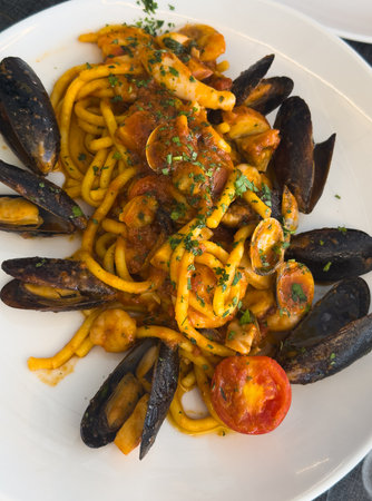View of a round plate of Italian seafood pasta garnished with half a tomato on a trattoria table in...