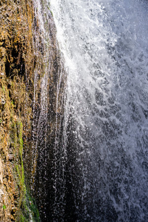 Close-up of a strong waterfall cascading down a textured rock wall, capturing movement, energy,...