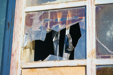Damaged window with torn plastic sheet and taped cracks. Urban decay, abandonment, renovation need...