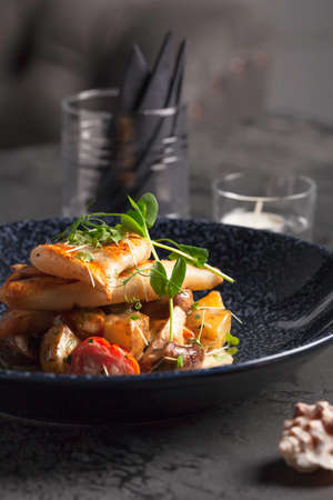 Restaurant menu. Seafood with baked potatoes. Calamari and shrimp on the grill. Cherry tomatoes with micro-green sauce. Ceramic ware.の写真素材