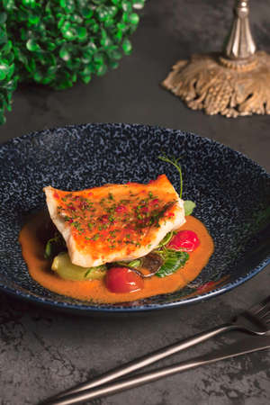 Restaurant menu. Juicy grilled fish fillet with bright orange sauce with cherry and micro greens. The blue plate. Dark backgroundの写真素材