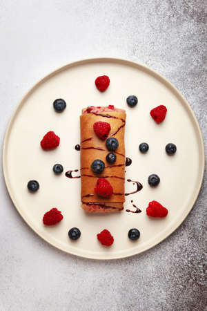 Homemade pancake with berry filling, poured with caramel and decorated with fresh berries-raspberries and blueberries on a white ceramic plate to pancake weekの写真素材