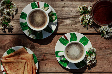 Coffee cups with pancakes with spring flowers on a wooden background