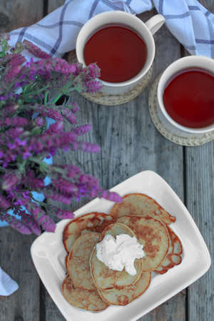 Breakfast with pancakes. Mini pancakes with flowers. Purple flowers in a pot. Pancakes with creaの写真素材