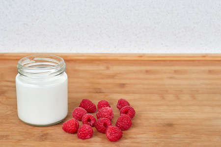 Yogurt in glass jar and raspberries on a wooden background - on the left sideの写真素材