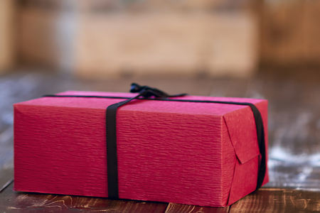 Red Christmas gift decorated with black ribbon and bow on a wooden tableの写真素材