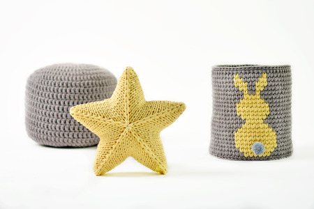 Yellow knitted five-pointed star shaped pillow, knitted basket with yellow rabbit and padded stool on white backgroundの写真素材