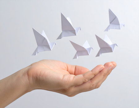 In a serene moment, a person's hand gracefully releases a flock of delicate origami birds into the air. The gentle light of twilight creates an enchanting atmosphere as dreams take flight.の素材