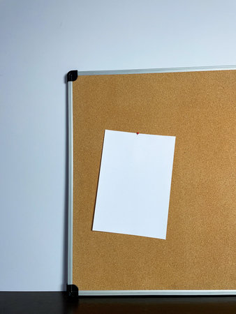 A cork board hangs on a light blue wall with a single, blank white note pinned to it, ready for...