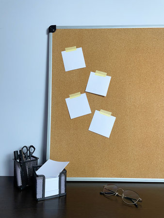 A tidy workspace shows a cork bulletin board with paper notes, a pen holder, a note cube, and...