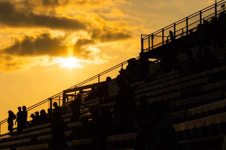 People sitting and standing on bleachers with golden sunset