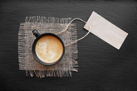 Coffee cup on rustic burlap and blank paper card. Top view with copyspace for your text. black background, cappuccino. price tagの写真素材