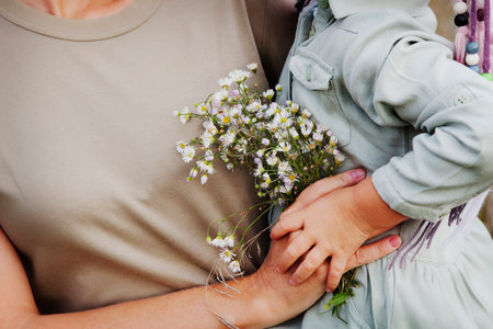 Close up Details. Hands of woman and child. Mom holds her daughter with daisies flowers. Natural color, copy spaceの写真素材